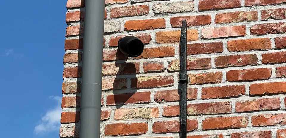 Bewakingscamera op een bakstenen gevel naast een regenpijp