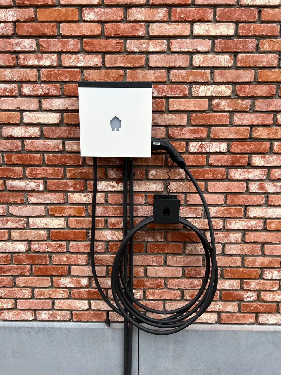 Wandlaadpaal met opgerolde laadkabel op een rode bakstenen muur