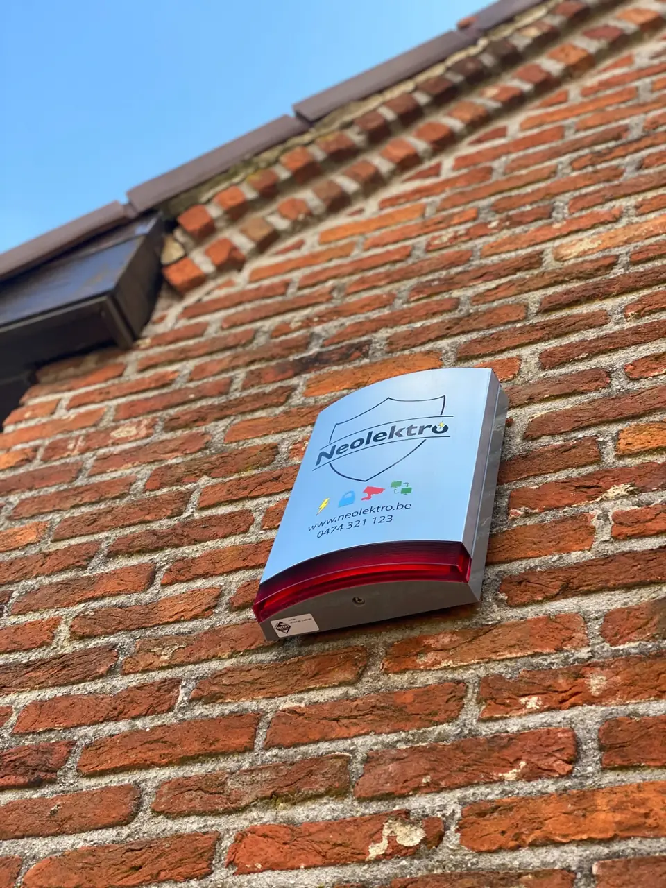 Buitensirene met flitslicht en Neolektro-logo op een bakstenen gevel